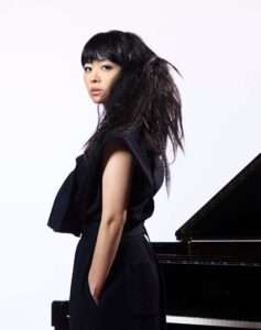 Hiromi Uehara seated beside a piano