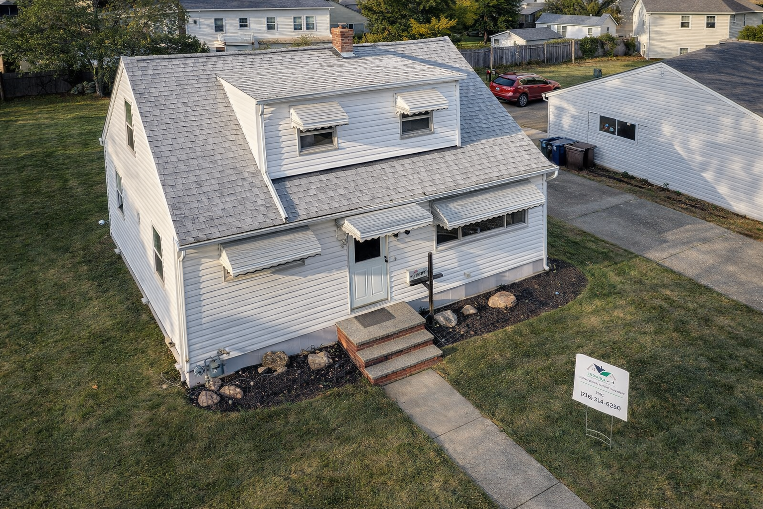 Completed roof project on a white cape cod home with Kronika Construction yard sign — Northeast Ohio