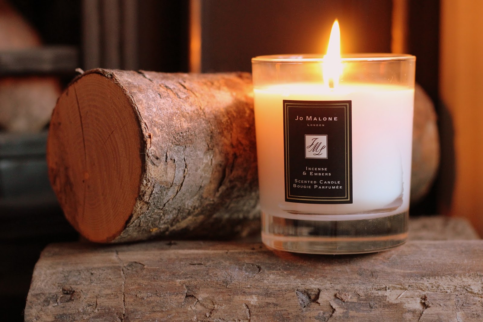 Jo Malone candle burning beside a log on a rustic wood surface