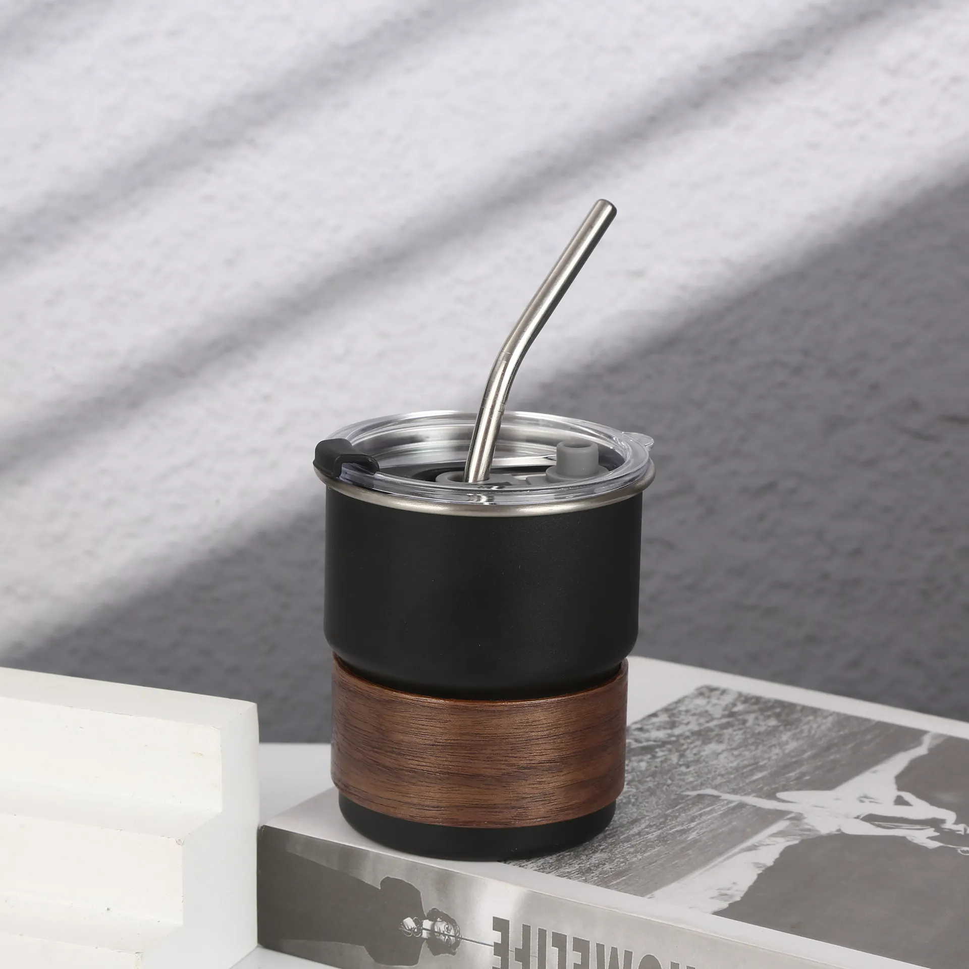Stainless steel coffee cup with wooden wrap sitting on books in natural light