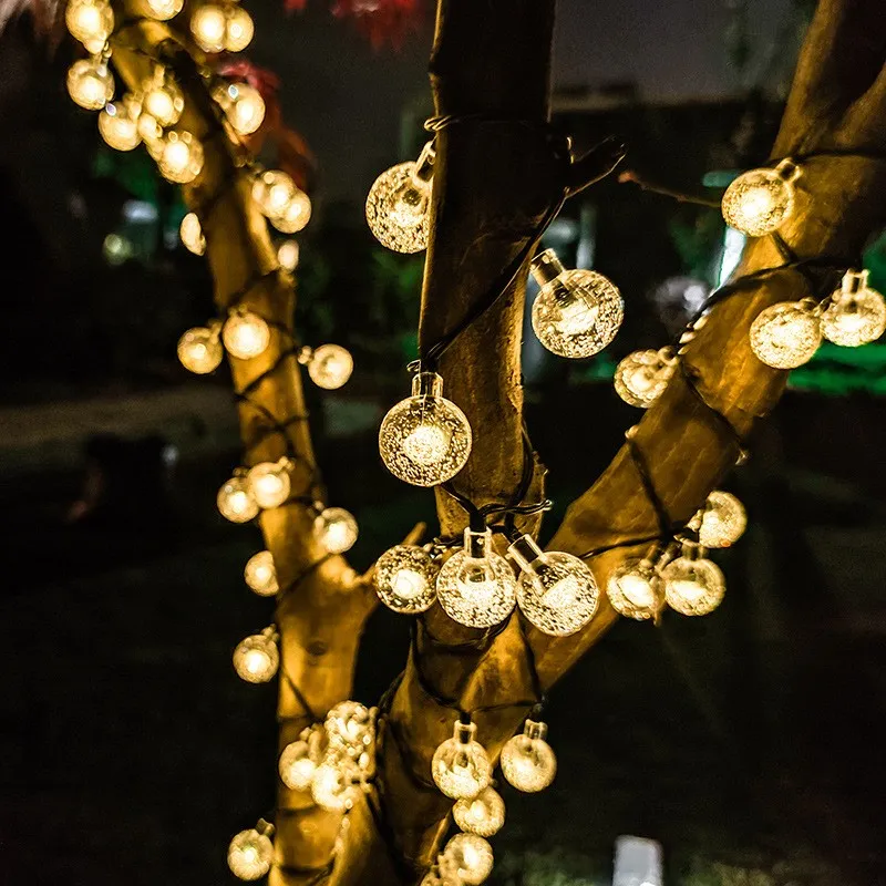 Warm white bubble ball solar string lights wrapped around a tree and hanging along a garden fence
