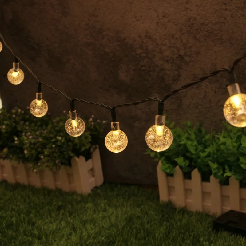 Warm white bubble ball solar string lights wrapped around a tree and hanging along a garden fence