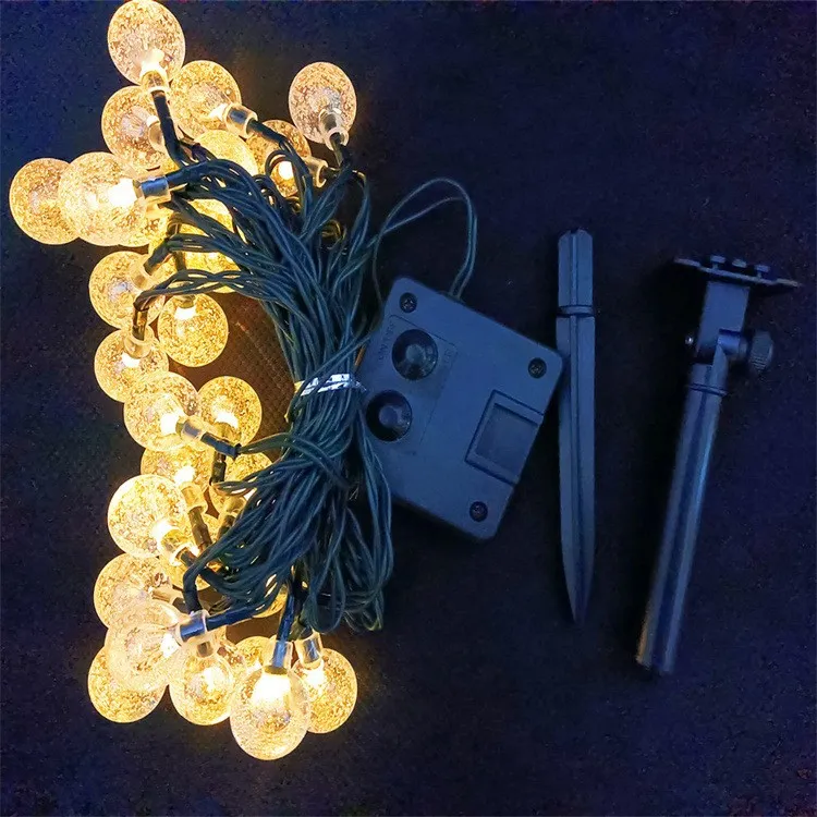 Warm white bubble ball solar string lights wrapped around a tree and hanging along a garden fence