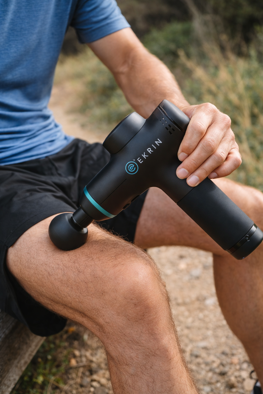Man using an Ekrin Athletics B37 massage gun on his knee on a trail