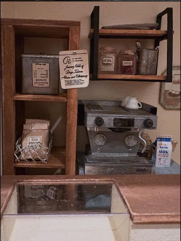 Close view of a miniature cafe counter with a small machine, shelves, jars, and paper bags