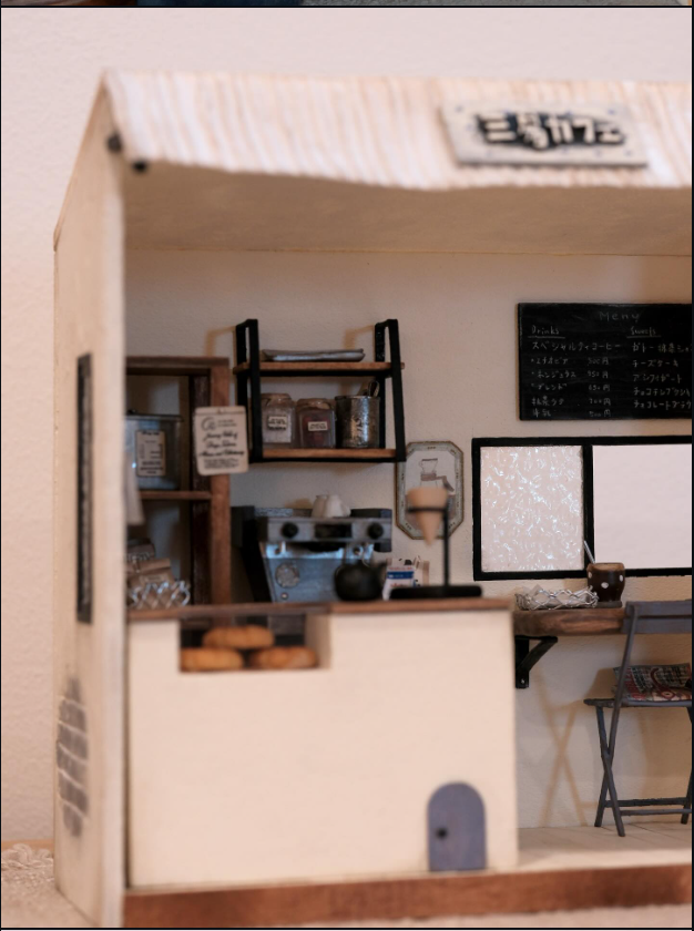 Wider view of a miniature cafe facade with a signboard, counter, and window seating