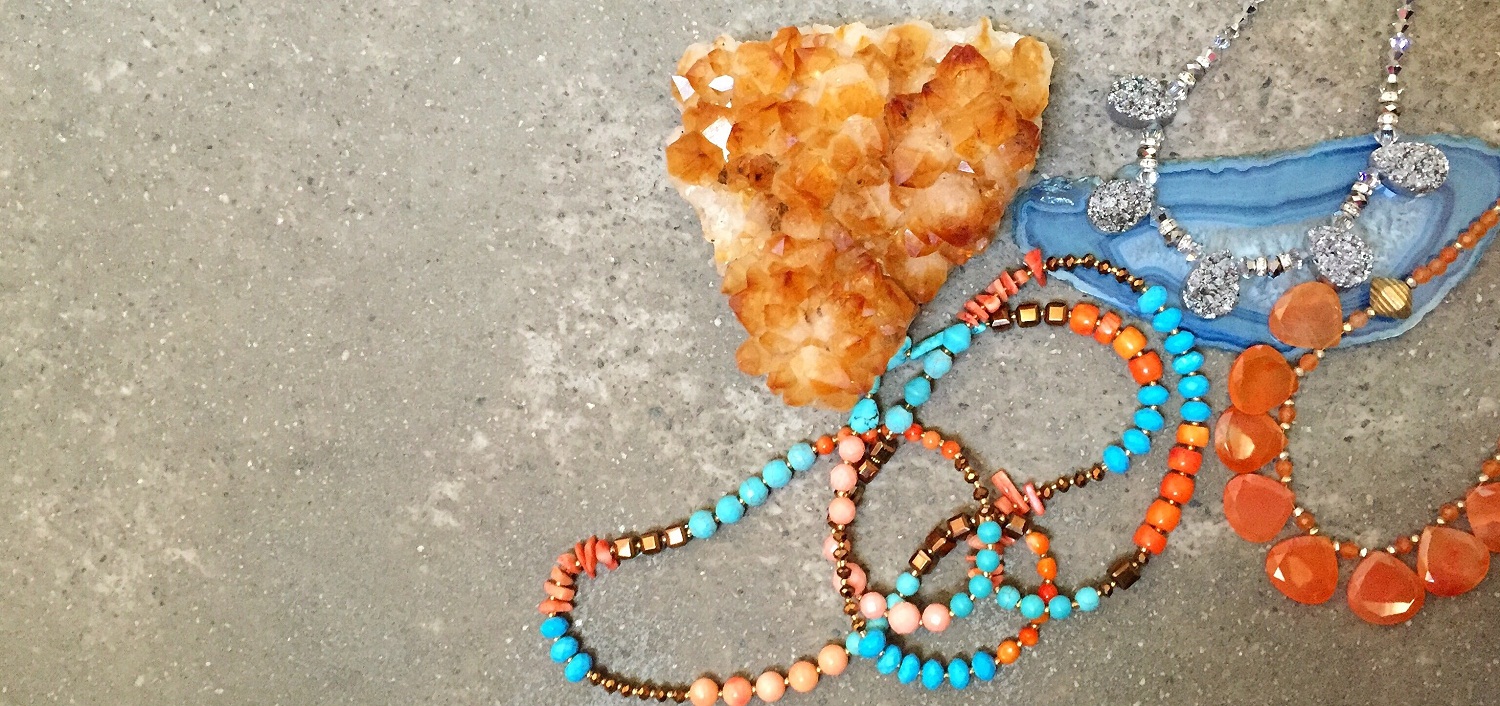 Citrine crystal cluster with colourful gemstone bead strands and a blue agate slice on a concrete surface