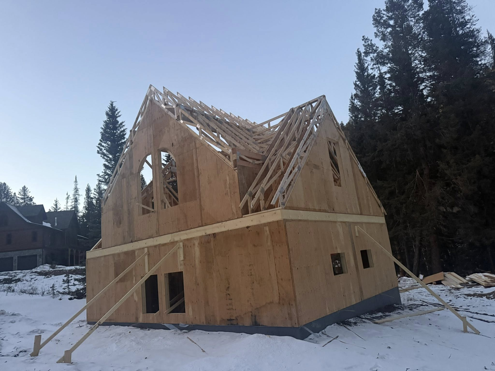 Custom home framing with exposed roof trusses in winter mountain setting