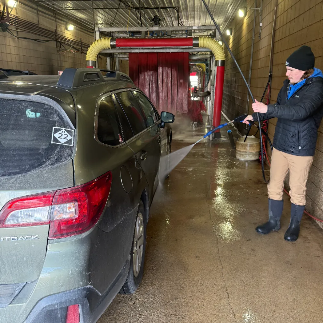 Staff member pressure-washing a vehicle before it enters the wash tunnel