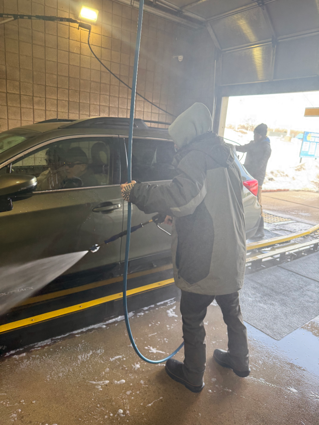 Employee using a pressure wand to clean the side of a vehicle
