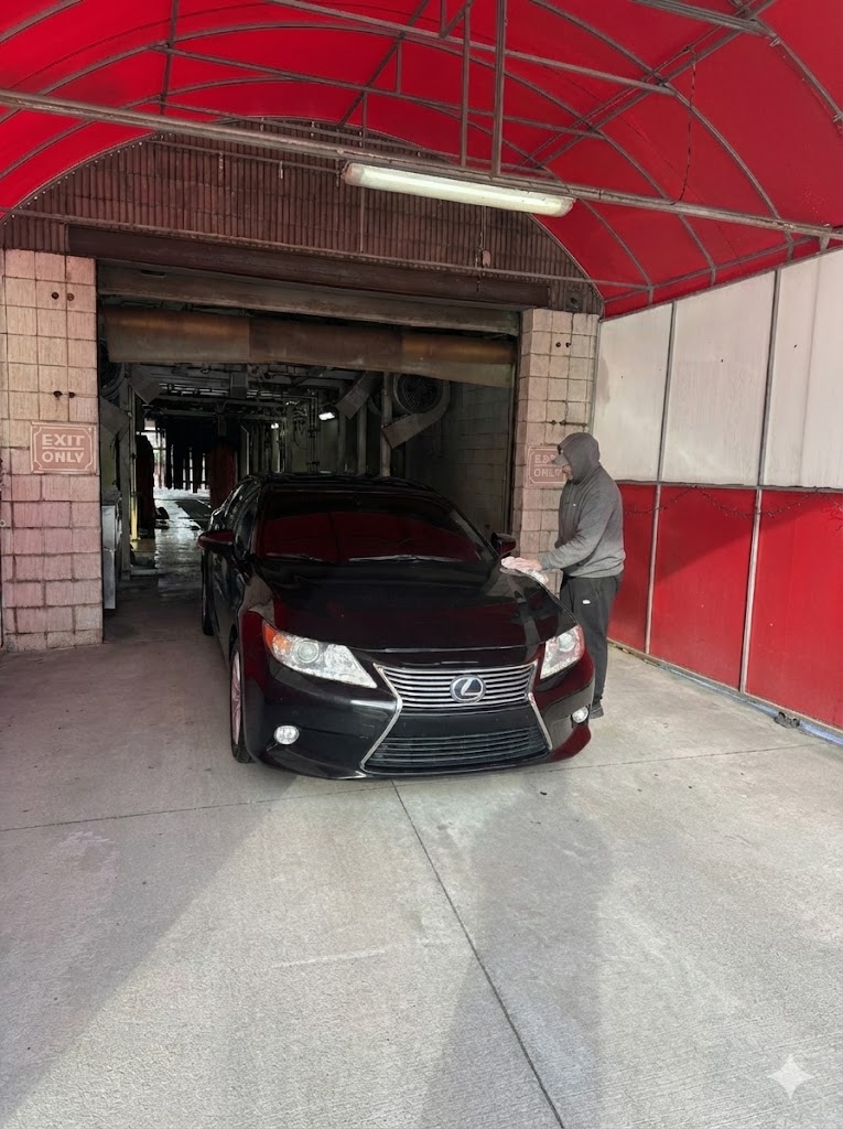 Team member power washing a black car inside the tunnel