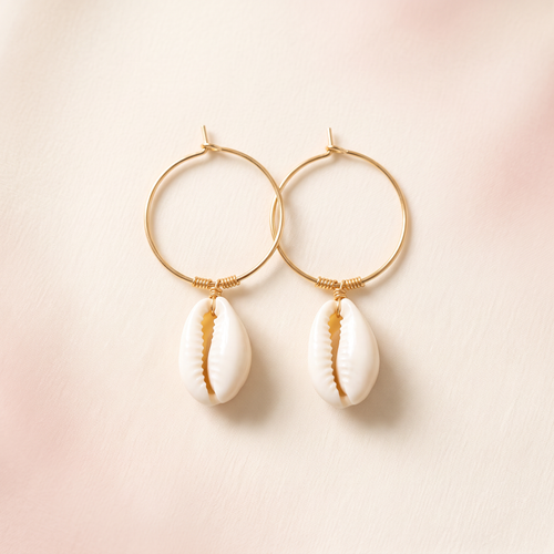 Pair of thin gold hoop earrings with white shell-like drop charms on a warm ivory and blush background