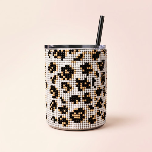 Black-and-white leopard-print beaded tumbler with gold accents, black lid, and straw on a soft blush and ivory background