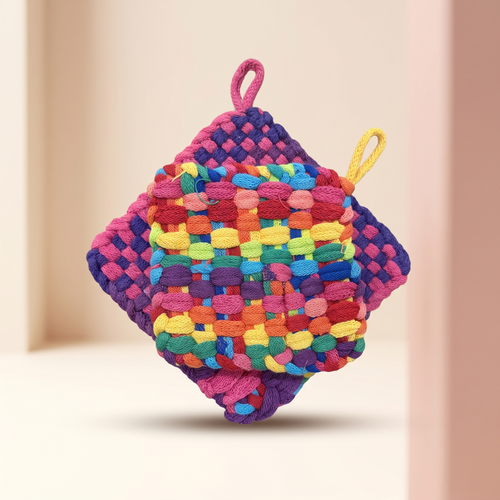 Two colorful woven pot holders stacked together on a softly lit warm ivory and blush-pink boutique background