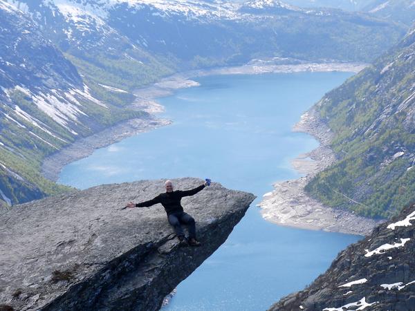 Person sitting on a rocky cliff above a mountain lake