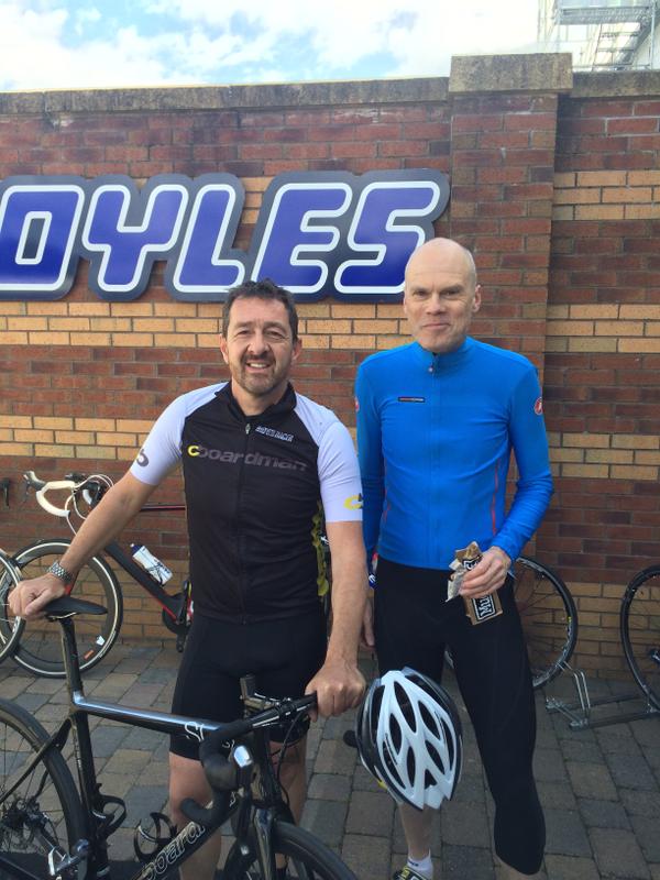 Two cyclists standing beside their bikes outside a brick building