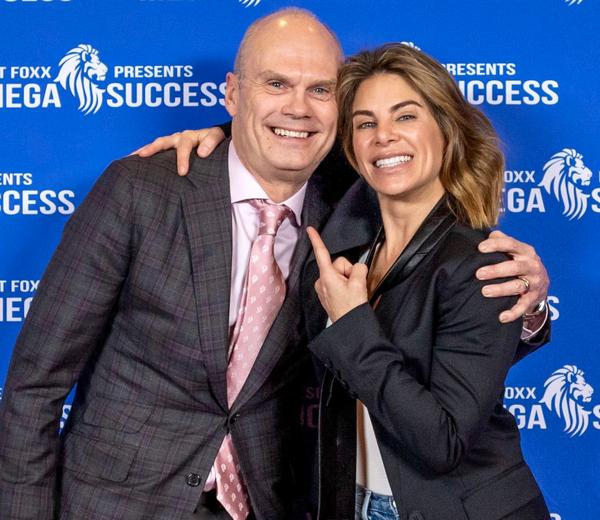 A suited man and a woman smiling together before a blue event backdrop