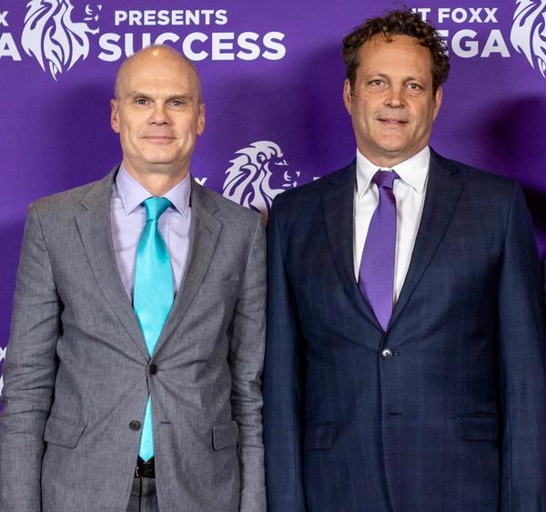 Two men standing beside a table displaying chess pieces at a business event