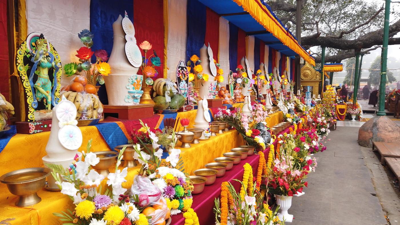 Colourful shrine displays with flowers, lamps, and devotional figures beneath a covered pavilion.