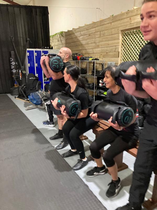 Warrior Fitness class members performing a seated weighted conditioning exercise in the gym.