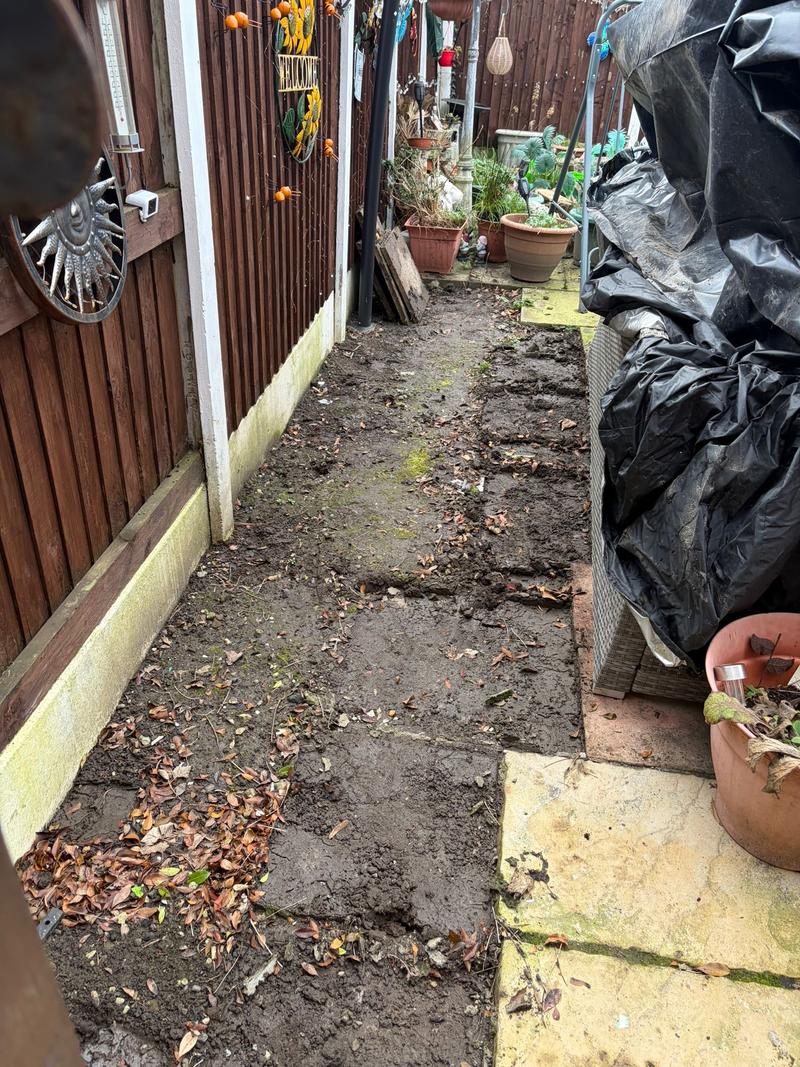 Before photo of a muddy side passage beside a fence