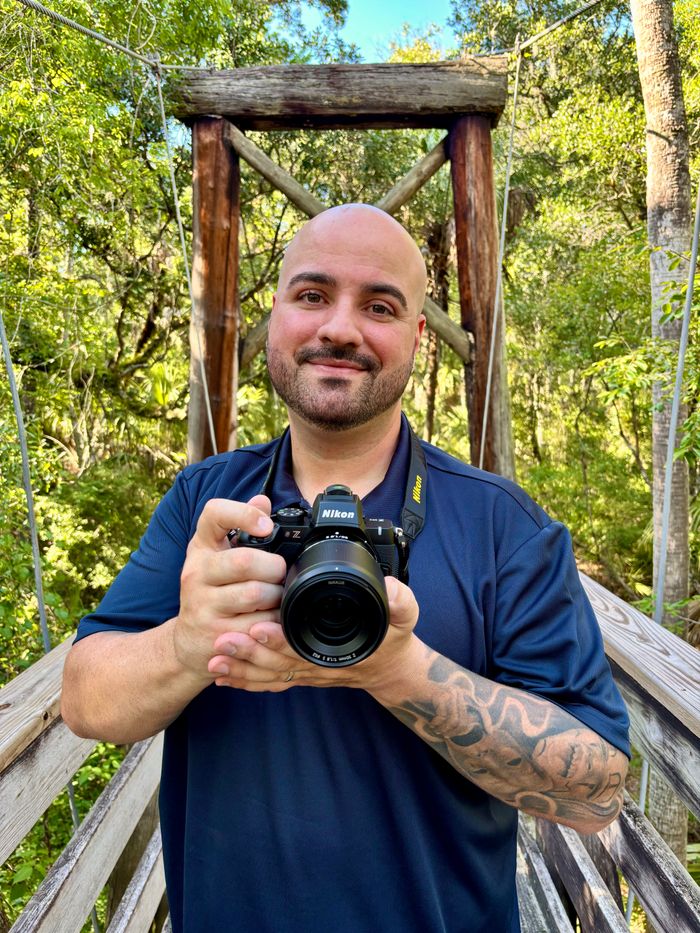 Thiago Navarro smiling outdoors while holding his Nikon camera