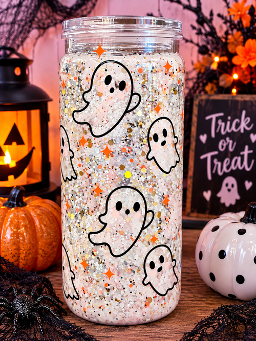 Clear glitter tumbler decorated with white ghosts and orange stars beside pumpkins, a lantern, and Halloween decor
