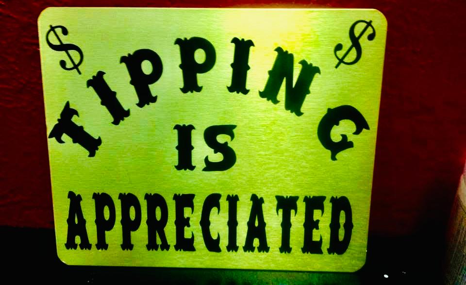 Lime-green sign with black Tipping Is Appreciated lettering and dollar signs, photographed against a red and dark background.