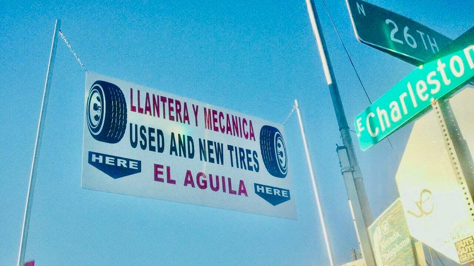 Roadside sign advertising new and used tires beside a street sign under a blue sky.