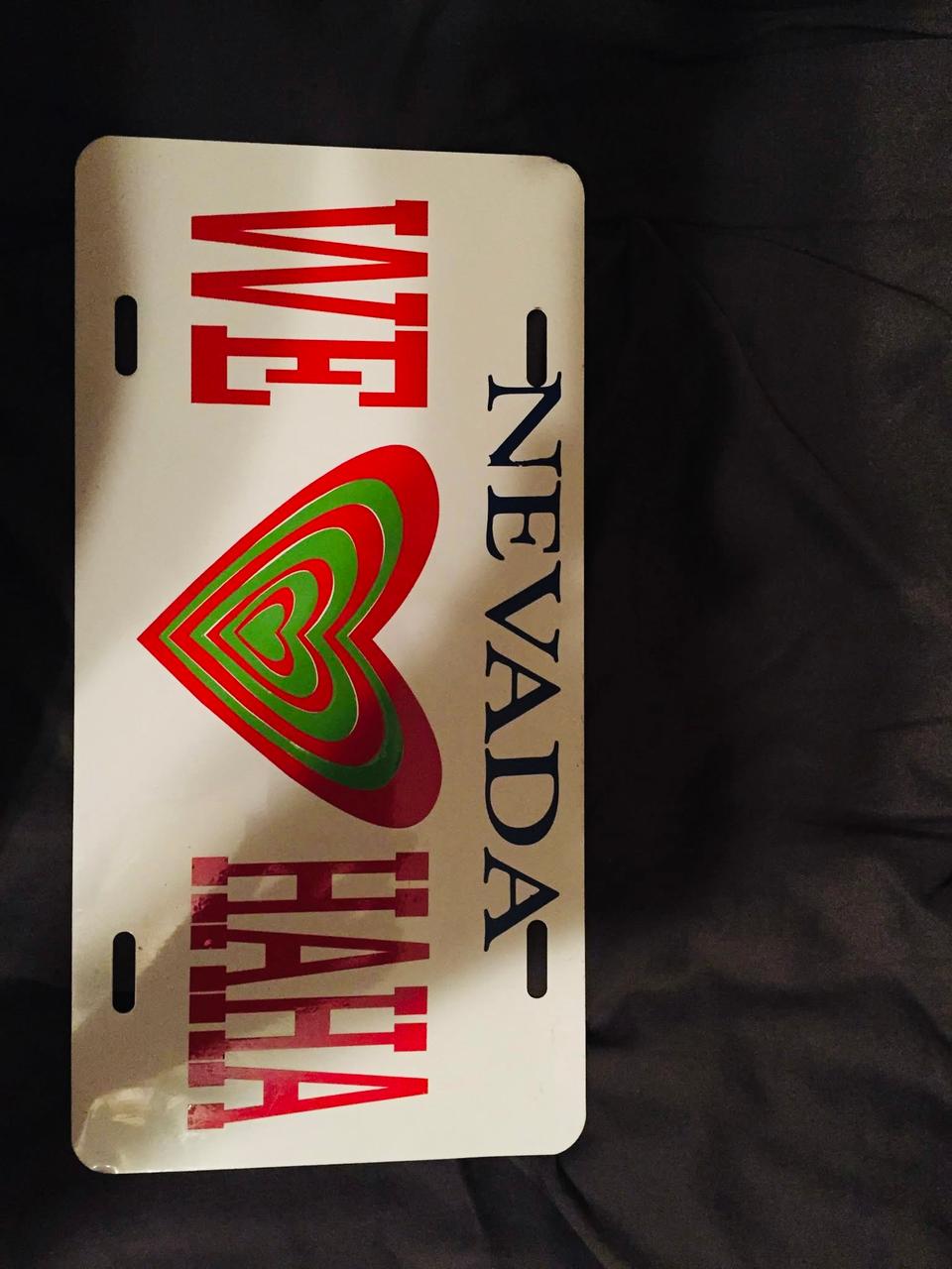 White plate-shaped sign with a red-and-green layered heart and Nevada lettering, photographed against a dark background.