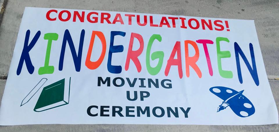 White celebration banner reading Congratulations and Kindergarten Moving Up Ceremony, with multicolored lettering and school-themed artwork.