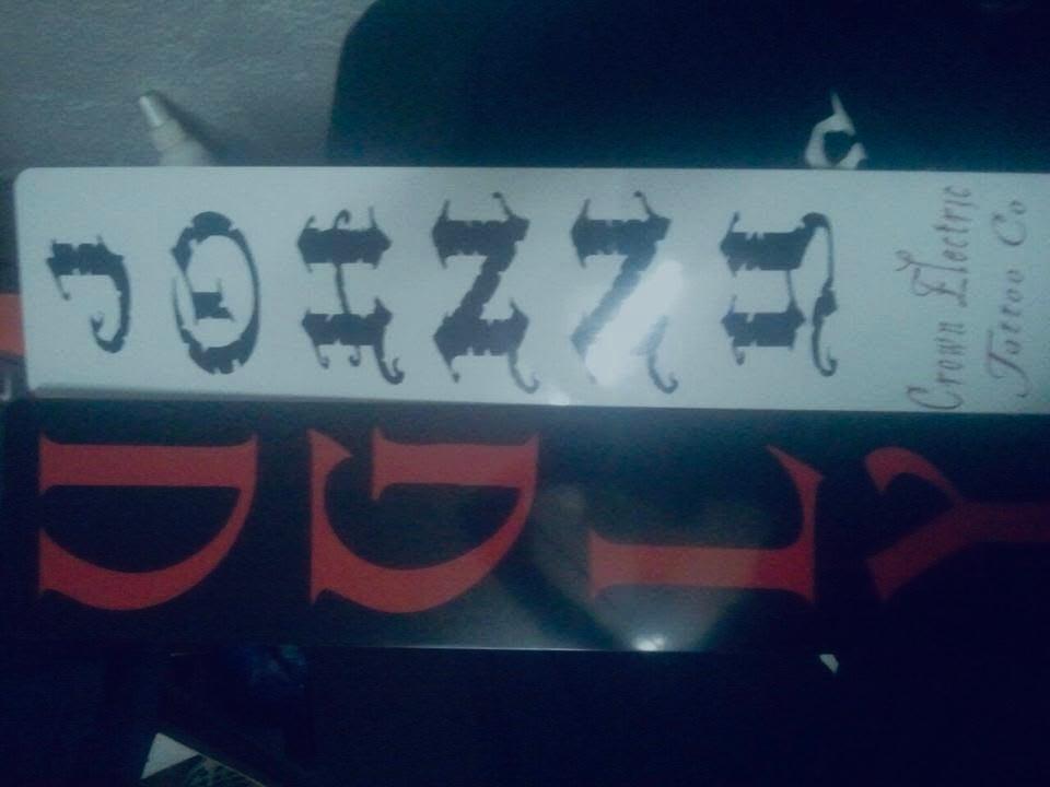 Narrow white sign with ornate black JESUS lettering, photographed sideways against a dark background.