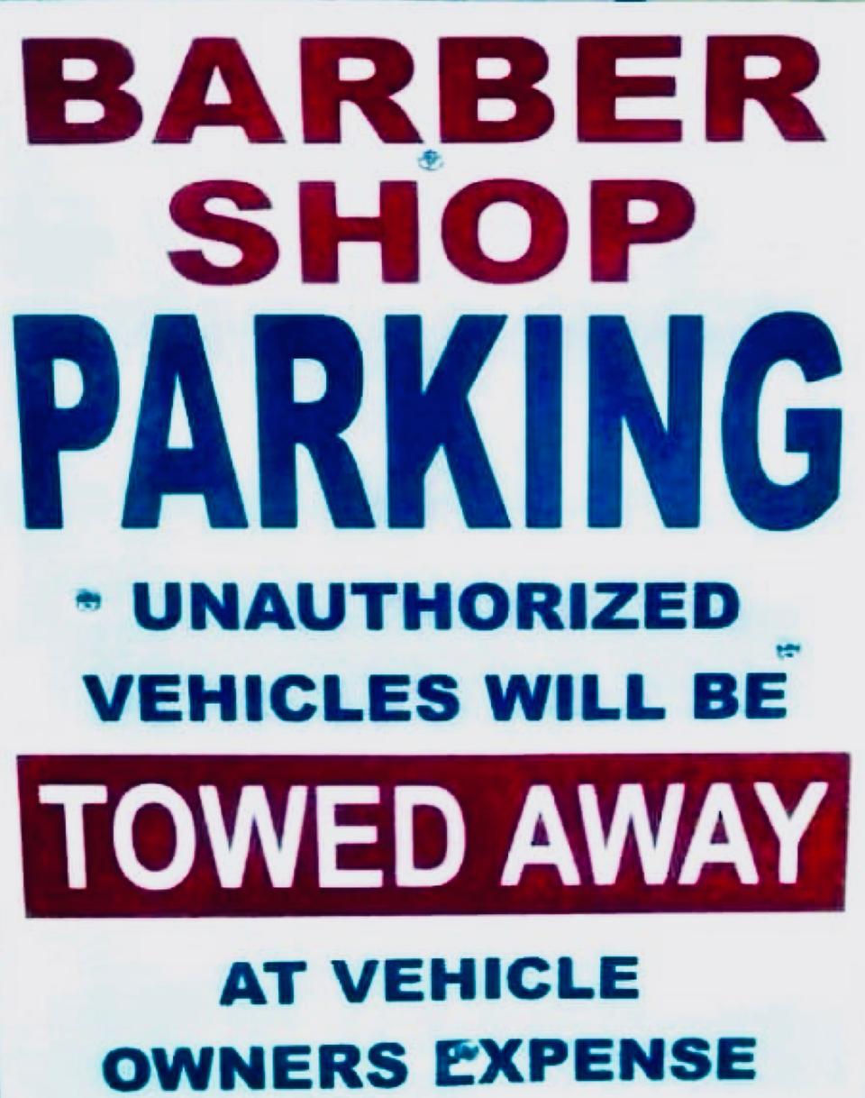 White Barber Shop Parking sign warning that unauthorized vehicles will be towed away at the vehicle owner's expense.
