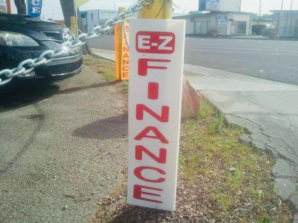 Tall white roadside sign with vertical red EZ Finance lettering beside a street.