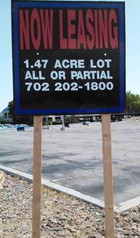 Black and blue roadside sign reading Now Leasing, 1.47 Acre Lot, All or Partial, and 702 202-1800, shown on wooden posts.