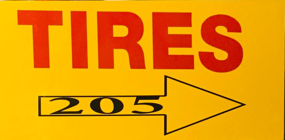 Bright yellow sign panel with red TIRES lettering and a black right-pointing arrow marked 205.