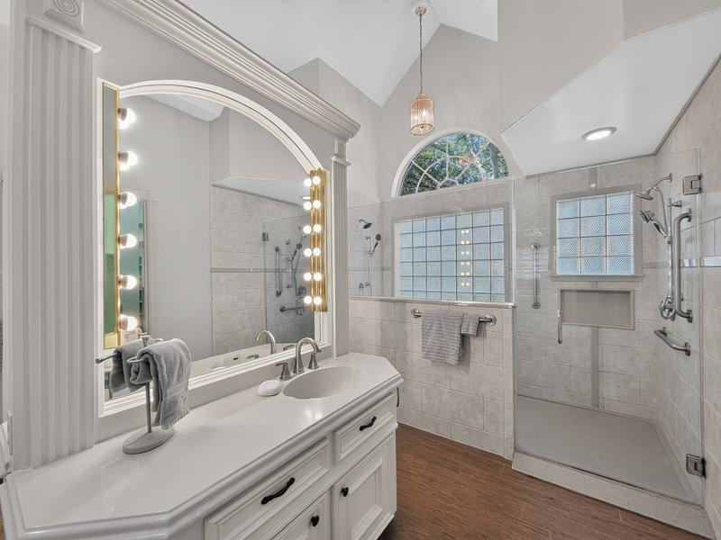 Bright bathroom with an arched mirror, long vanity, bathtub, and glass shower.