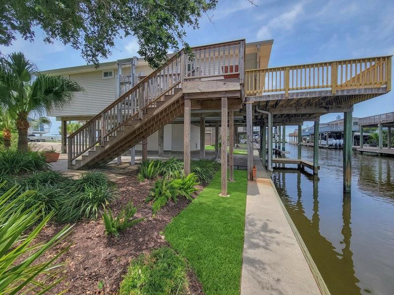 Raised waterfront home with a broad deck and dock beside the water.