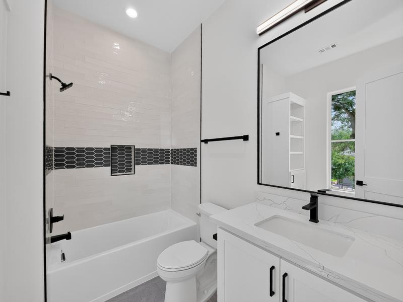 Bright bathroom with a bathtub, vanity, and dark tile accent.