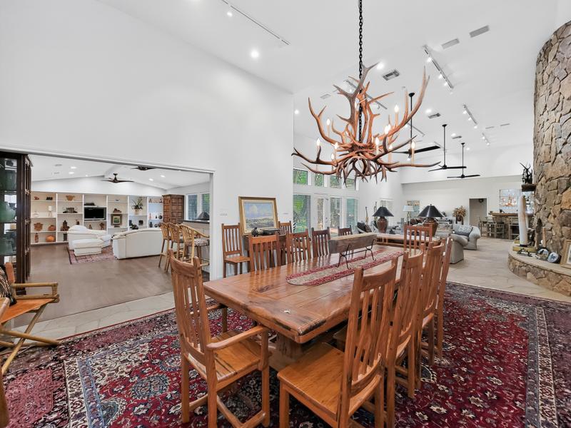 Dining area with a long wood table, chandelier, and open kitchen.
