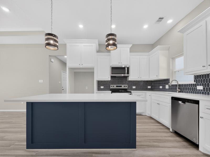 White kitchen with a deep blue island and dark tile backsplash.