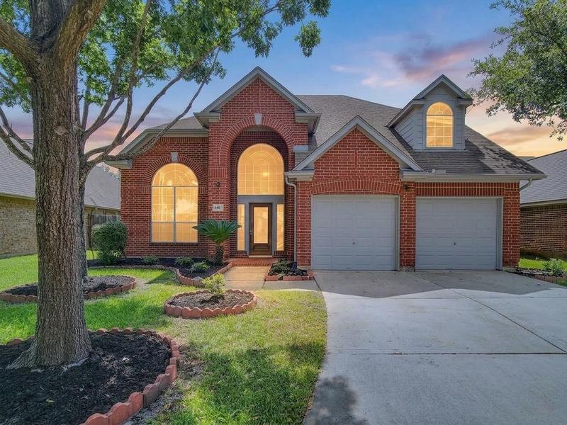 Brick home exterior with lit windows, a front lawn, and driveway.