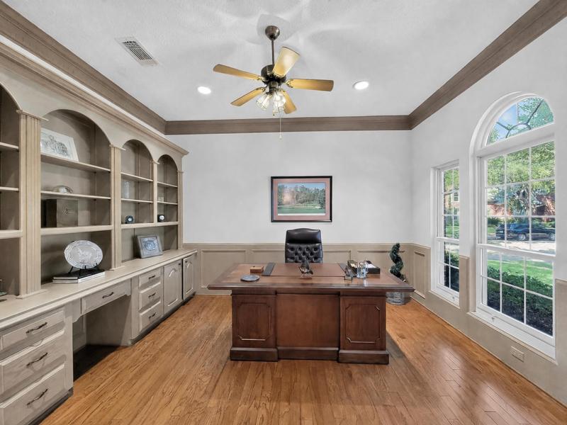 Home office with built-in shelving, a desk, and tall windows.