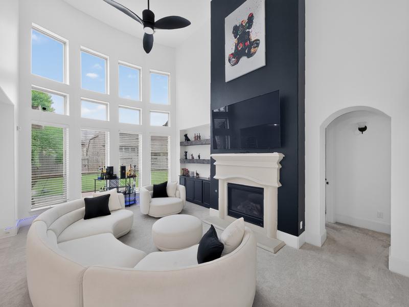 Living room with white seating, a dark fireplace wall, and tall windows.