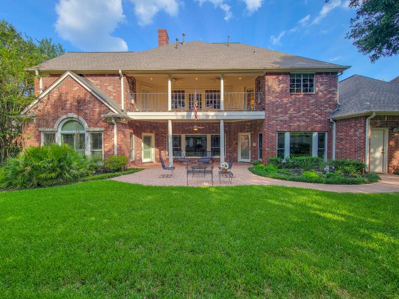 Brick home exterior with a lawn, patio, and upper balcony.
