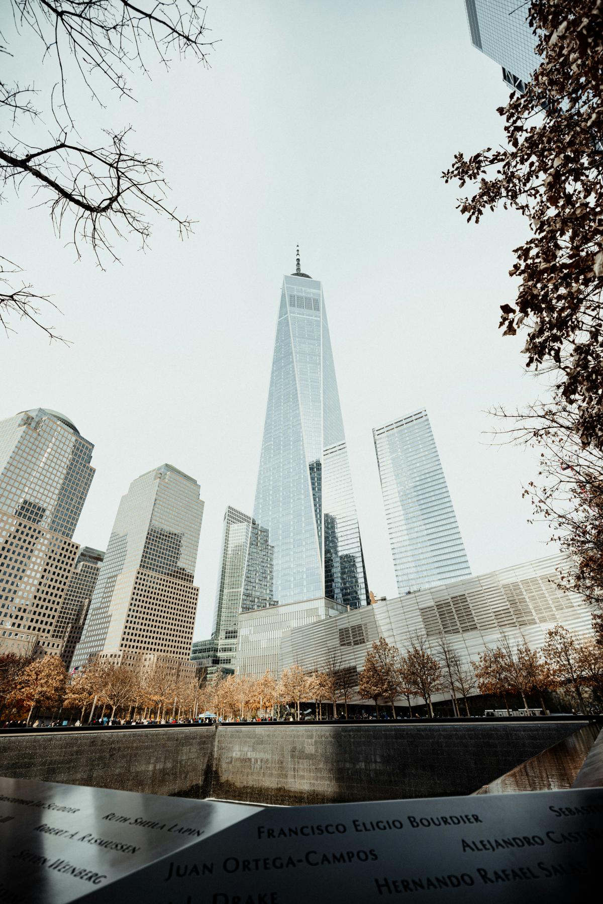 One World Trade Center rising above the 9/11 Memorial reflecting pool, with engraved names in the foreground.